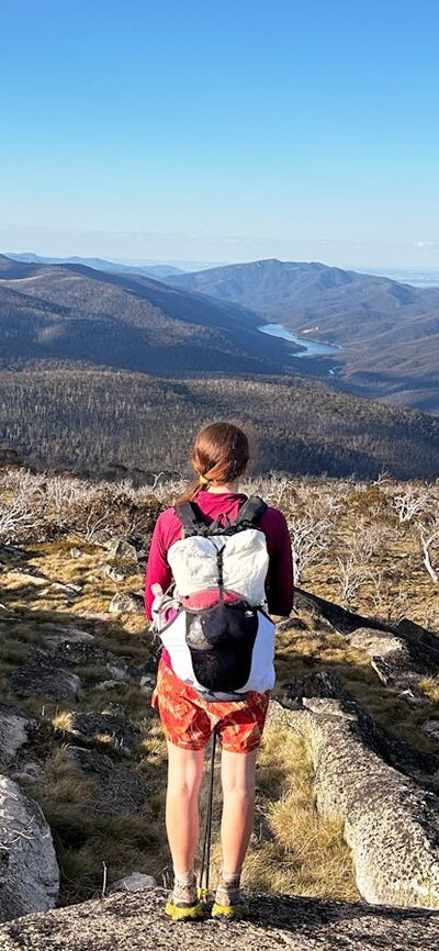 A hiker at the top of the mountain looking down onto a lake in the distance.