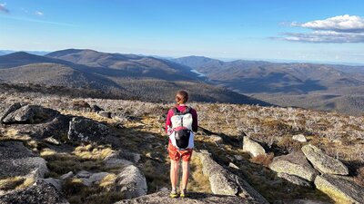 A hiker at the top of the mountain looking down onto a lake in the distance.