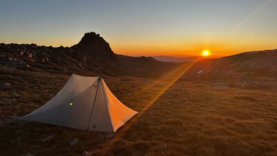 A tent on the mountains with the sun setting behind it.