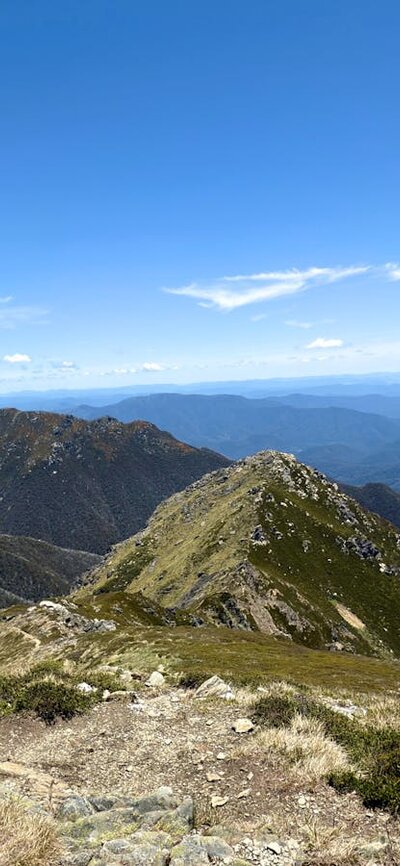 A narrow ridge with mountains in the distance and a blue sky.