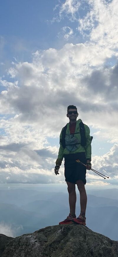 A hiker standing on a rock with clouds behind them.