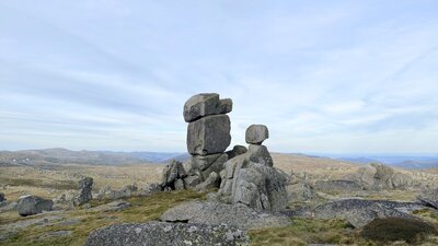 A stack of boulders in an open field in the mountains with an overcast sky.