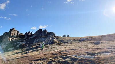 A hiker walking up a slope in the mountains with some jagged rocks behind them.