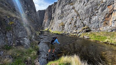 A hiker hopping across some rocks to cross a river in a gorge.