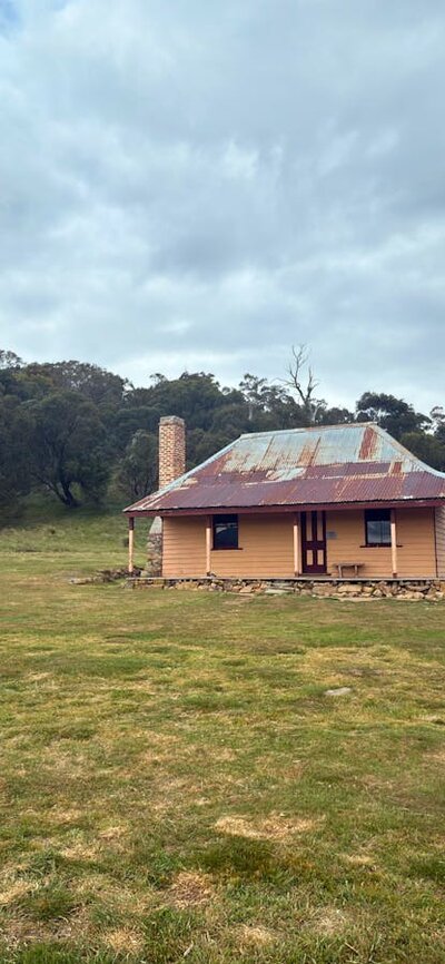 A hut in open terrain with trees in the background and an overcast sky.