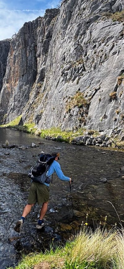 A hiker hopping across rocks to cross a river in a gorge.