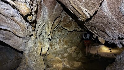 A cave with a tier walking through with a head torch.