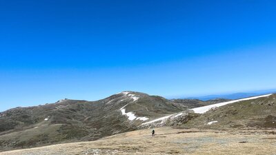 A hiker in the mountains climbing up a steady hill with snow in the background.