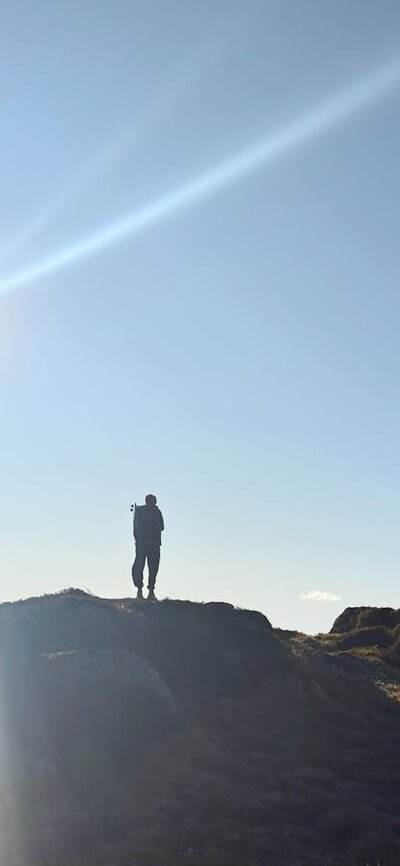 A hiker standing on a rock with the sun behind.