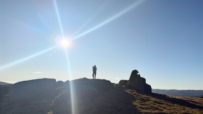 A hiker standing on a rock with the sun behind.