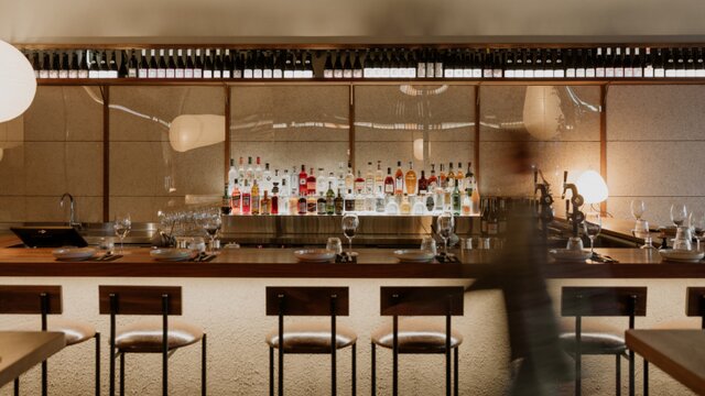 © Nathan Harradine-Hale Low-lit interior of a bar with bar stools and illuminated bottles on the wall at OHNO! in Manuka. | © Nathan Harradine-Hale