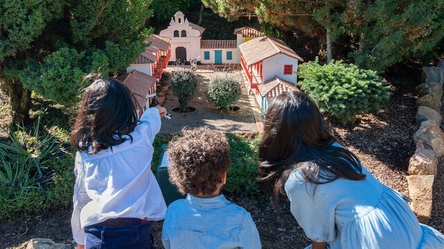 © Martin Ollman View of the backs of three children kneeling to look into a tiny house structure at Cockington Green Gardens. | © Martin Ollman