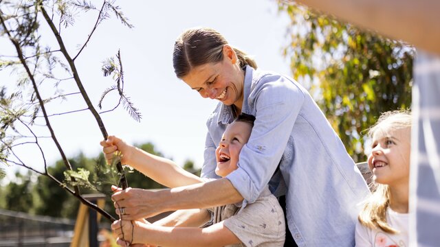 © Ken Leanfore Image of a smiling boy looking up at his smiling mum as they feed a giraffe leaves on sticks at the National Zoo & Aquarium. | © Ken Leanfore