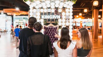 Four adults facing the brightly-lit interior of game venue, Kingpin.