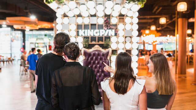 Four adults facing the brightly-lit interior of game venue, Kingpin.