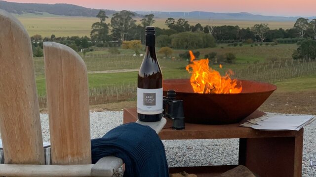 Lake George Winery accommodation | © Sarah McDougall View of a wine bottle by a fire pit at Lake George Winery's tiny house accommodation at sunset. | © Sarah McDougall