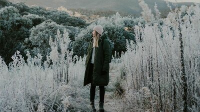 © @laurenlsutton Image of a blonde woman in a black jacket and beanie, standing in a frosty naturescape | © @laurenlsutton