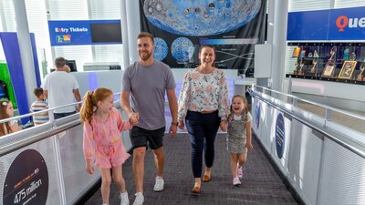 A family of a mum, dad and two daughters smiling as they walk up a ramp at Questacon