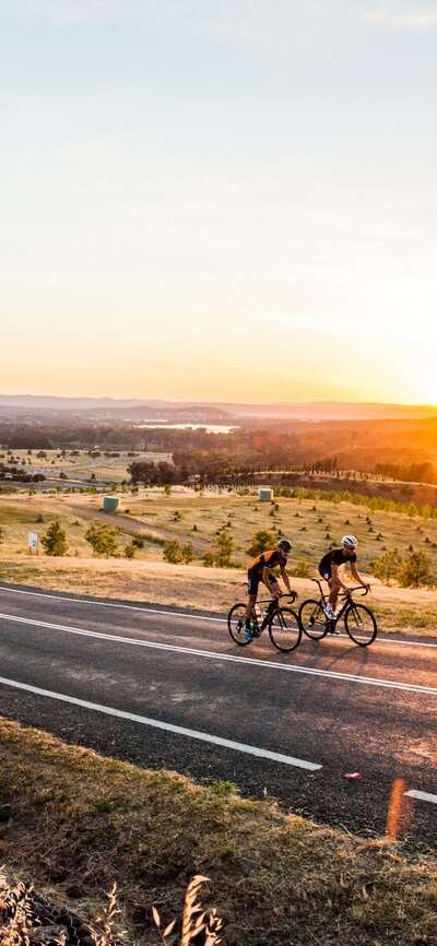 Two cyclists on the road with the National Arboretum Canberra and Telstra Tower seen in the background 