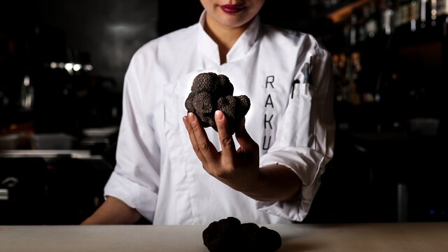 A chef of a Japanese restaurant holds a truffle to the camera.