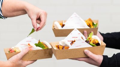 Three servings of Super Bao buns being held by customers on paper trays.