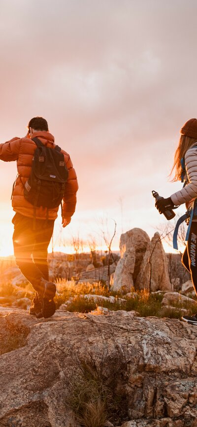 The backs of two people wearing activewear walking on the peak of a mountain. 