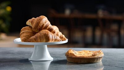 A buttery croissant and a flaky pie on a bench top.