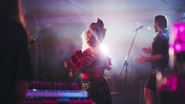 A woman wearing a costume with frilly sleeves, dancing on stage.