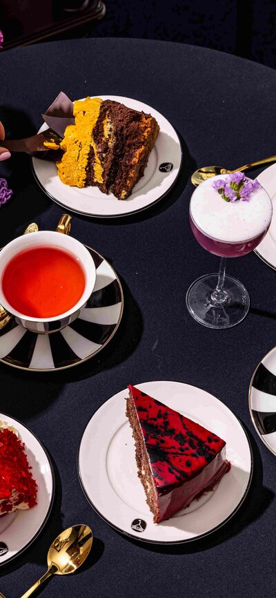 Hands reaching to grab various afternoon tea dishes on a table. 