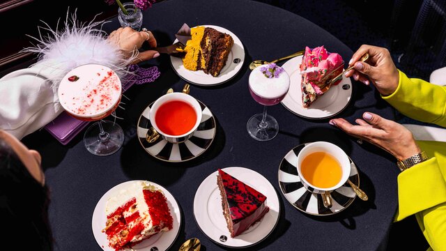 Hands reaching to grab various afternoon tea dishes on a table.