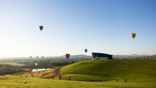 hot air balloons flying above lake and green hill