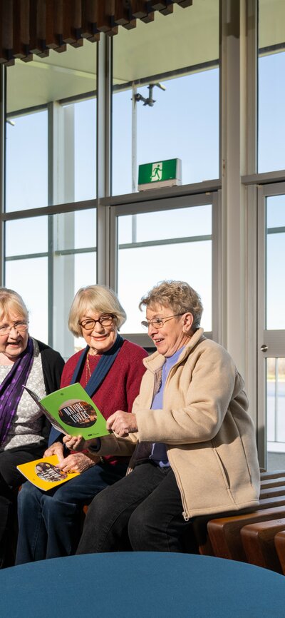 Three ladies reading from traveller brochures at a visitor centre.