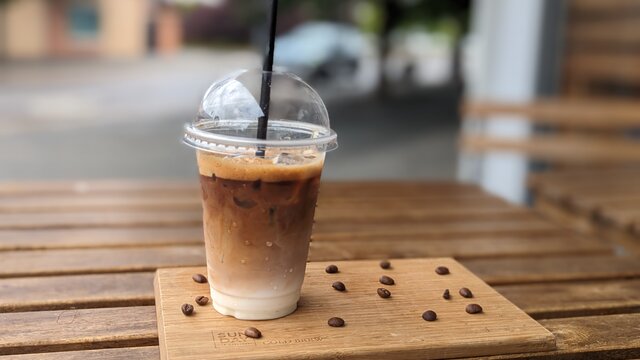 A Vietnamese iced coffee on a wooden board with coffee beans scattered on it.