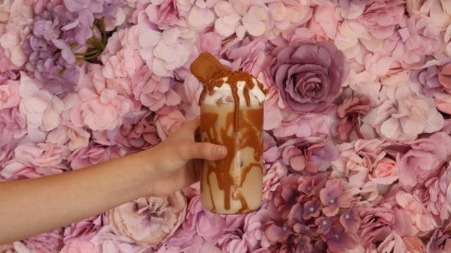 A loaded biscoff iced drink in front of a floral wall display.