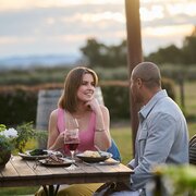 Man and woman having lunch outside with fields of vegetables growing in background