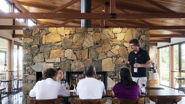 A person holding a bottle of wine and speaking to a group who are tasting wine