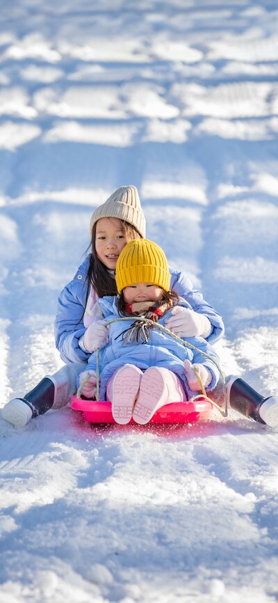 Two young girls ride on a toboggan together in the snow