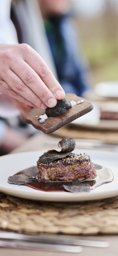 A hand shaving fresh truffle on a steak