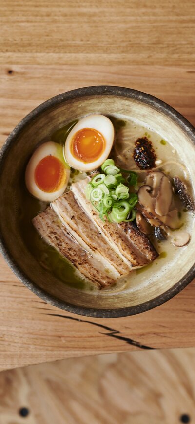 A bowl of traditional ramen with noodles. eggs, meat and vegetable