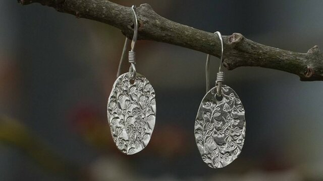 A pair of silver oval shape dangle earrings with a pattern on it