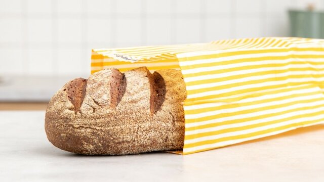 A half of a baguette bread stick peeping from a yellow striped wax bag