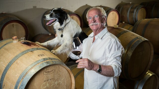 Ken Helm and dog Winemaker with glass and dog amongst wine barrels