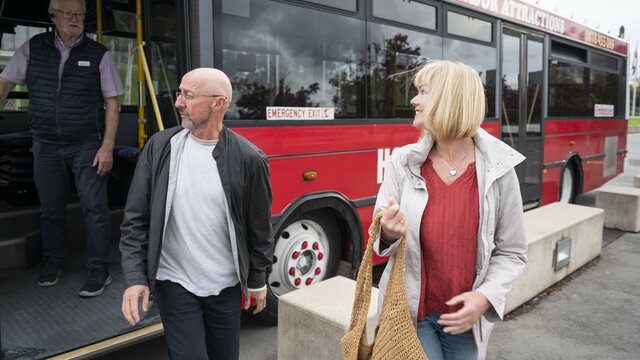 Two passengers departing a bright red bus with a bus driver in the background