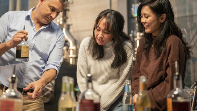 A person showing a bottle of gin to two participants on a tour group observing
