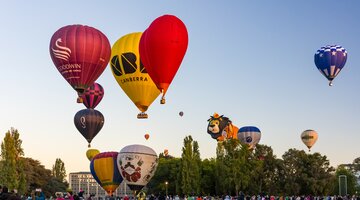 Various shapes and sizes of hot air balloons near the grounds with people watching the balloons