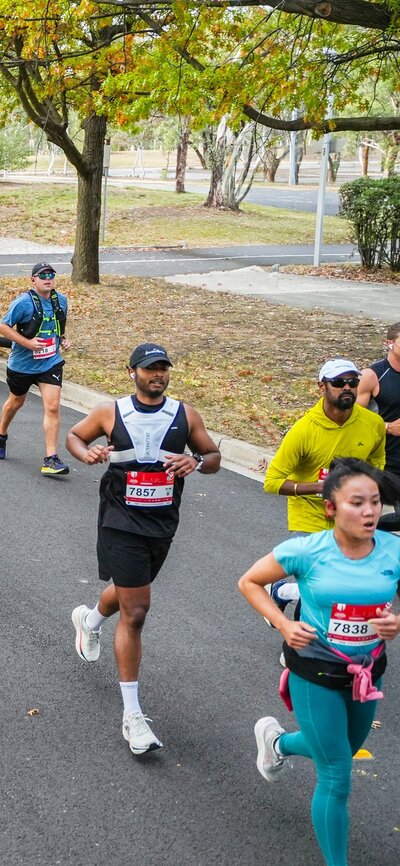 Canberra Marathon Running Runners taking part in the Canberra Marathon, running on a road under an inflatable archway with trees on both sides of the road.