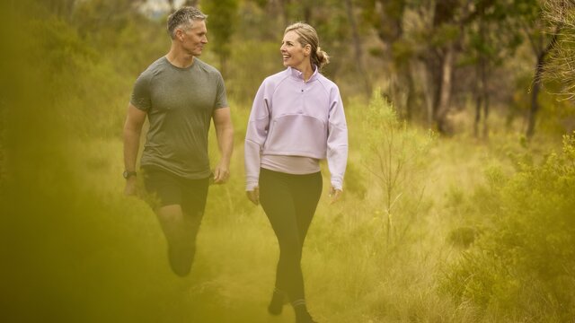 A man and woman walk through a nature park, smiling at each other
