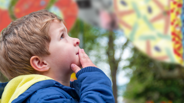 A small boy looking into the sky with colourful decorations in the background