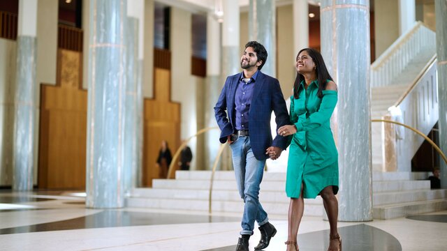 Two people holding hands walking through a large building with marble walls