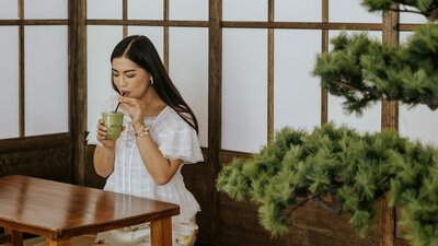 A woman sipping a matcha drink from a straw in a Japanese setting